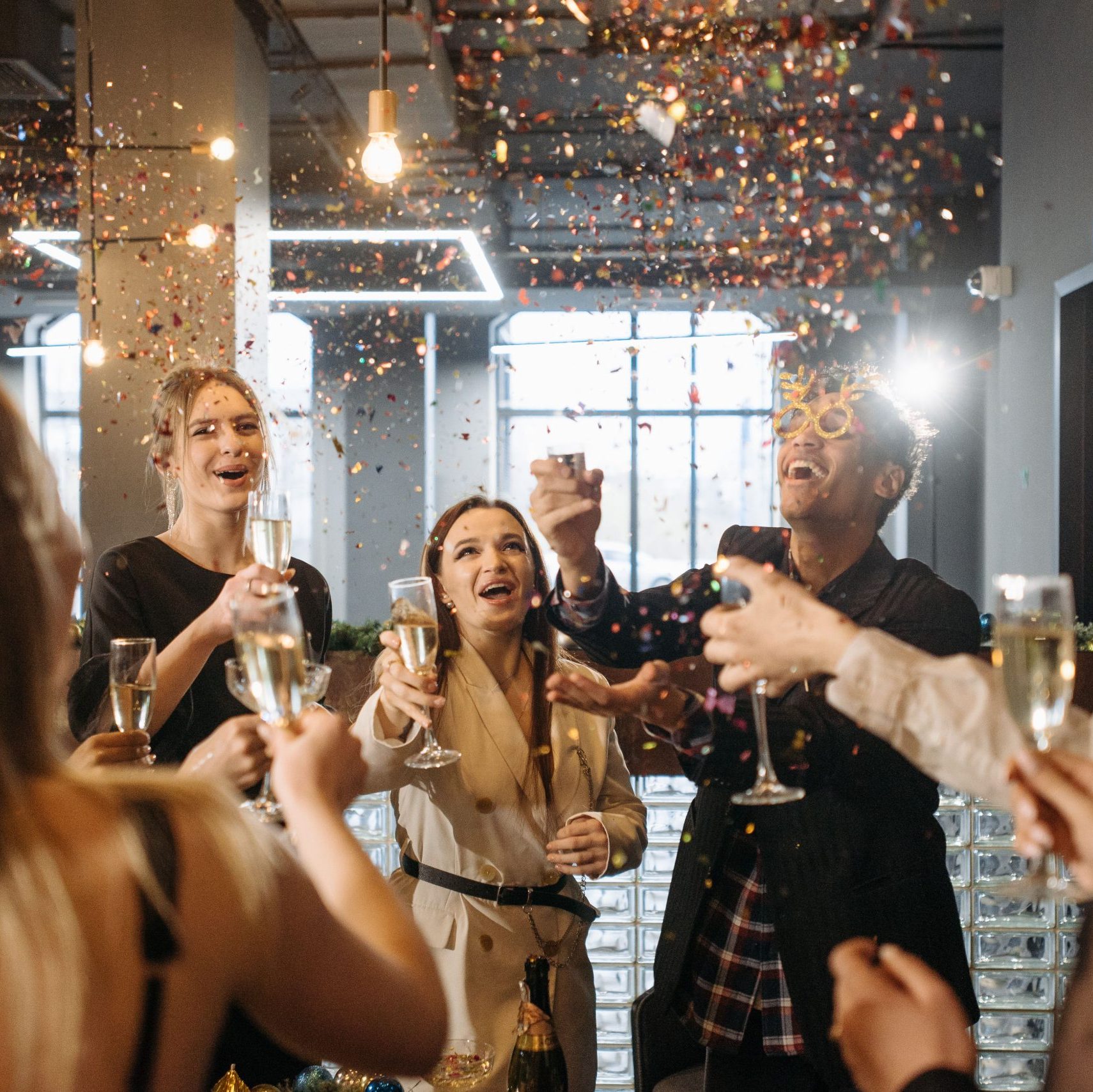 Home A group of friends celebrates indoors with champagne and confetti in a festive atmosphere.